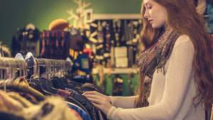 Side view of a woman in a shop looking through clothes hanging on a rail